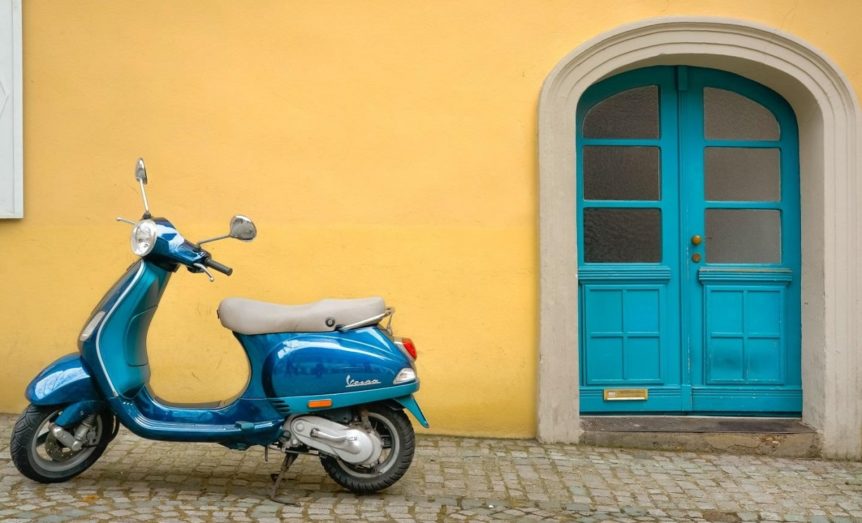 blue scooter parked next to a yellow wall